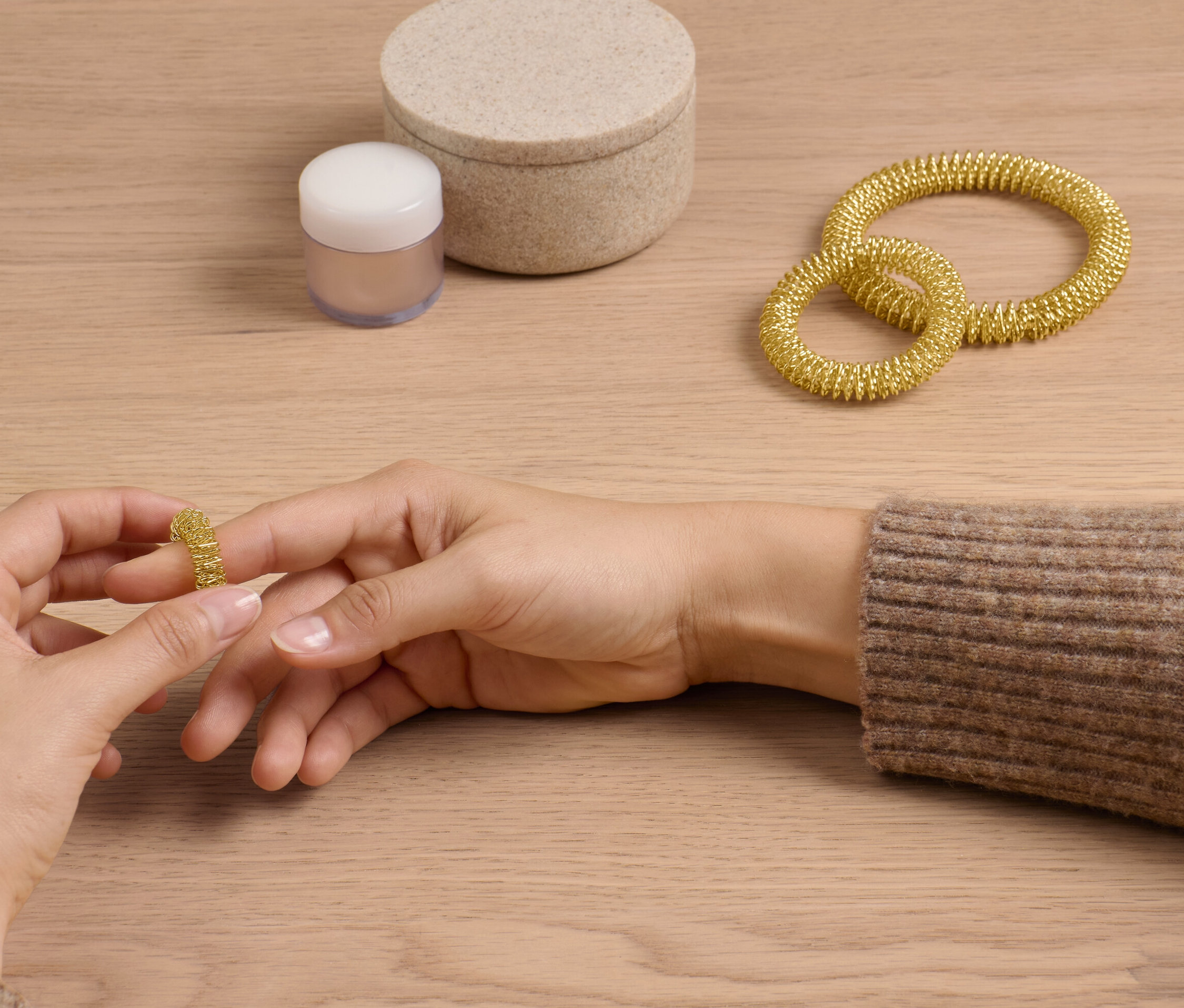 Žena si navlieka zlatý akupresúrny krúžok zo súpravy na prst. Na stole ležia ďalšie dva krúžky a škatuľka.