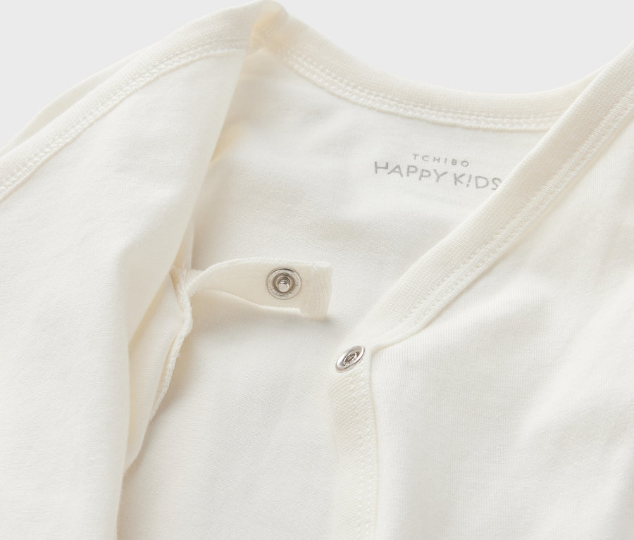 Detail bieleho body pre bábätká s možnosťou prispôsobenia veľkosti s patentkami.