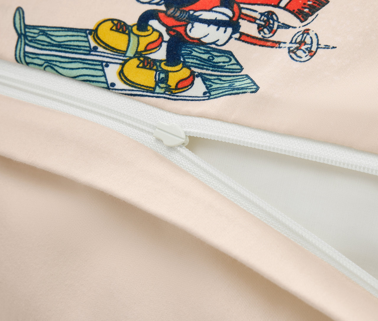 Detailný záber na obliečku na prikrývku s potlačou Mickey Mouse na lyžiach a čiastočne rozopnutým zipsom.