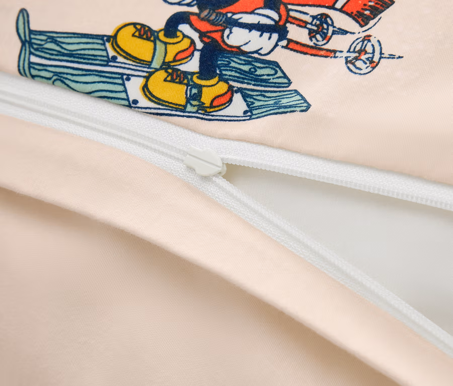 Detailný záber na obliečku na prikrývku s potlačou Mickey Mouse na lyžiach a čiastočne rozopnutým zipsom.