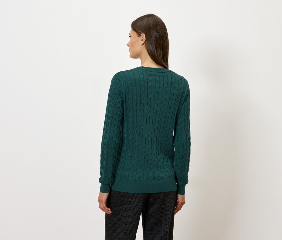 Pohľad zozadu na ženu v zelenom svetri a tmavých nohaviciach.