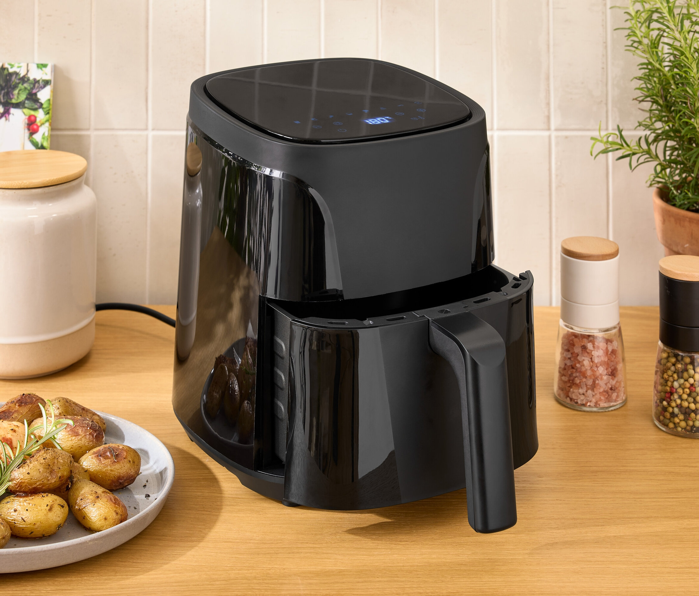 Čierna teplovzdušná fritéza na drevenom stole vedľa taniera s kuracím mäsom a zemiakmi.