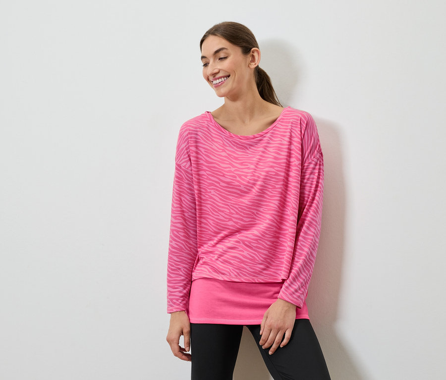 Usmievajúca sa žena pózuje v ružovom tope s dlhým rukávom a čiernych legínach.