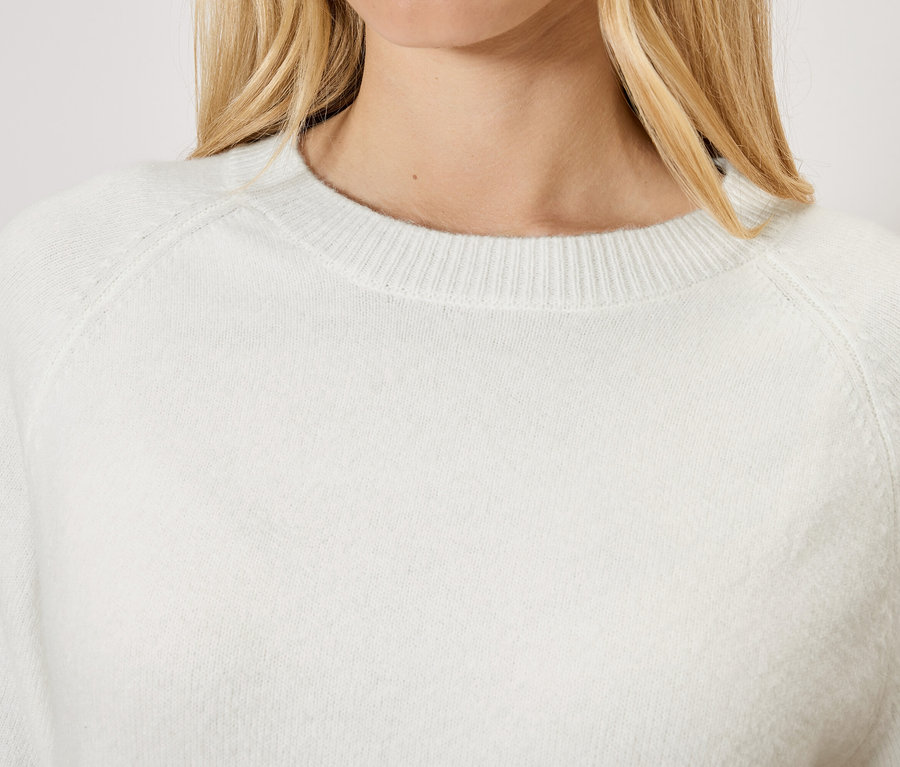 Žena s blond vlasmi má na sebe biely sveter.
