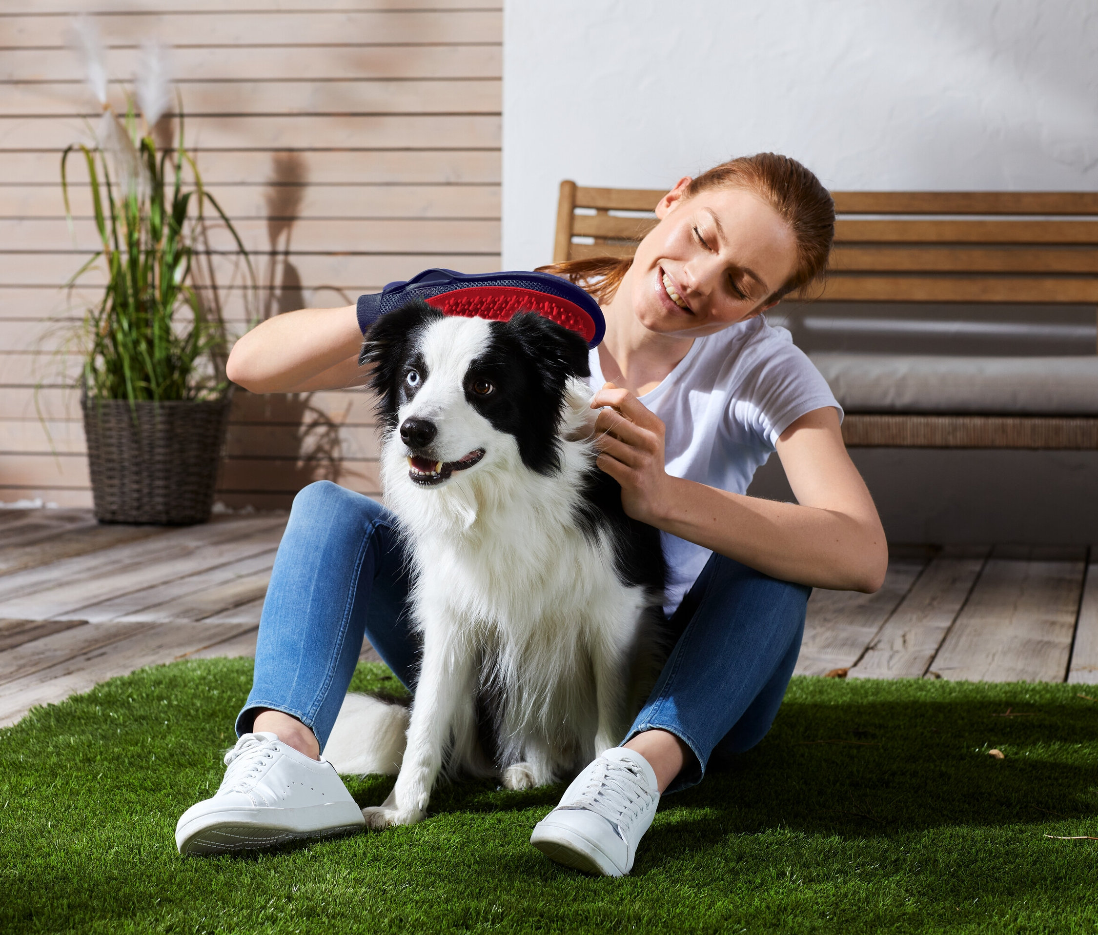 Žena sedí na tráve a kefuje čierno-bieleho psa.