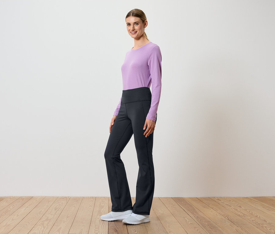 Žena pózuje bokom v lila tope s dlhým rukávom a čiernych nohaviciach s vysokým pásom.