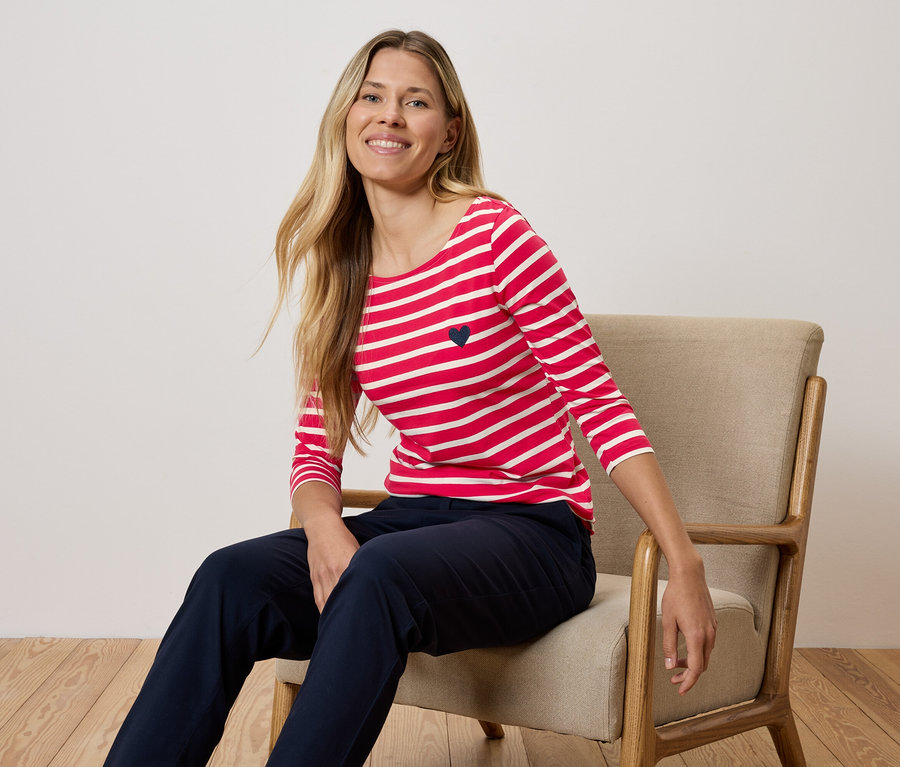 Žena sedí na stoličke a má na sebe červeno-biele pruhované tričko a tmavomodré nohavice.