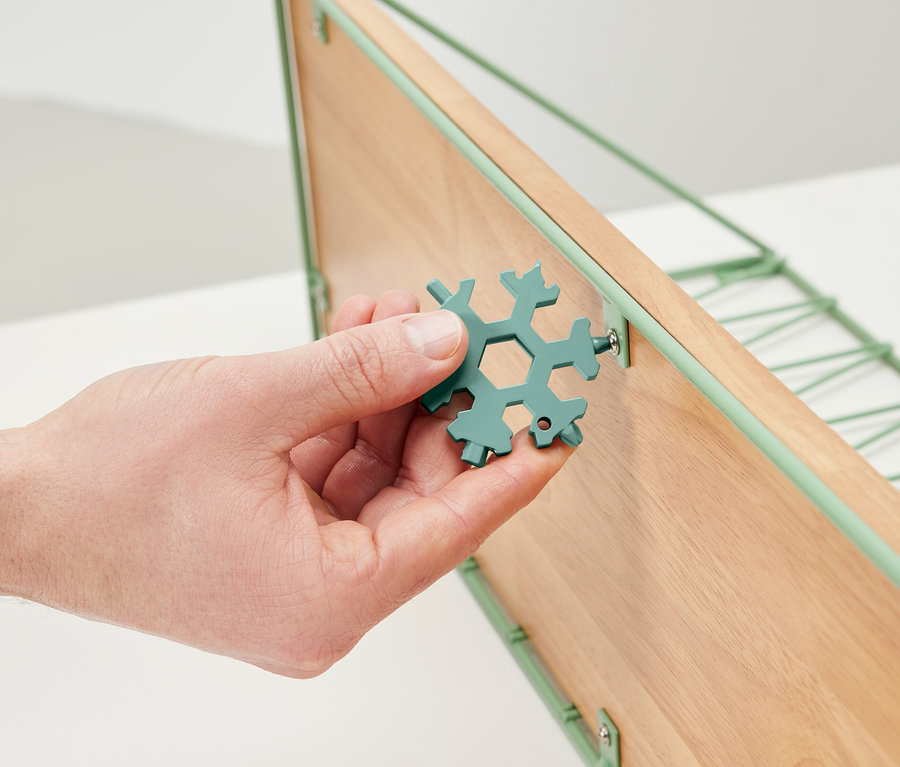 Ruka drží multifunkčný kľúč a uťahuje skrutku na drevenej polici.