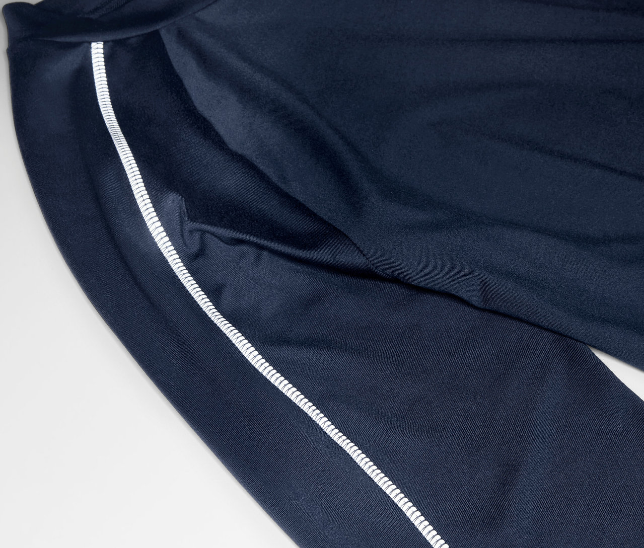 Detailný záber na tmavomodré tepláky s bielym pruhom na boku.