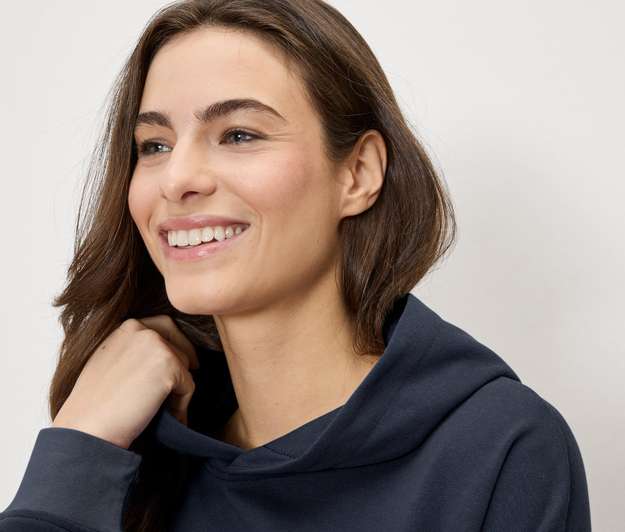 Žena sa usmieva a má na sebe tmavomodrú mikinu s kapucňou.