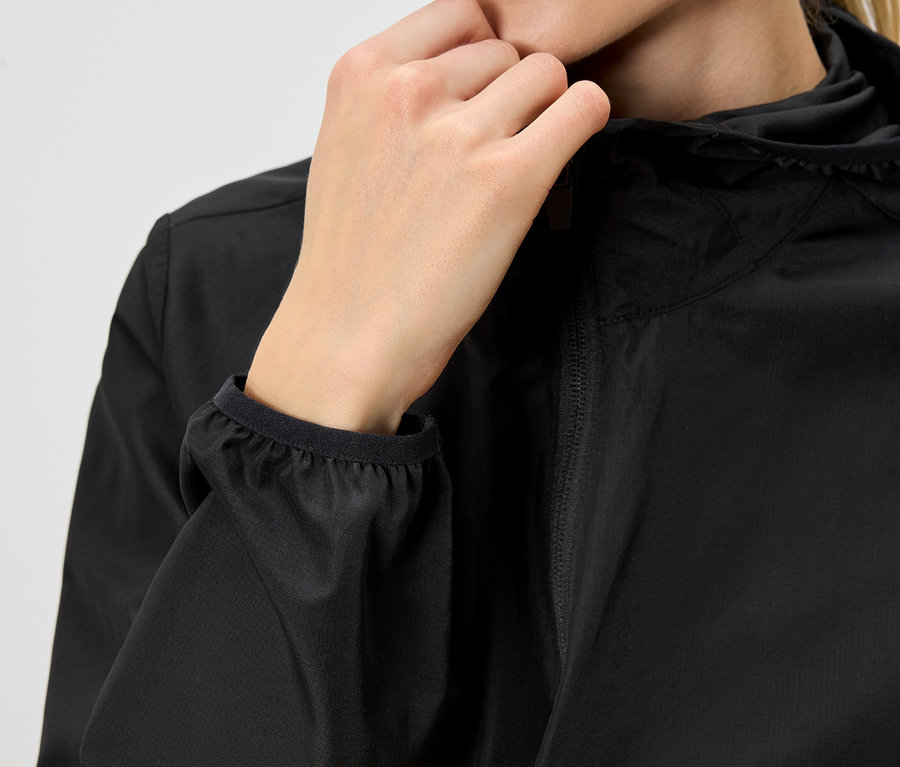 Detail osoby v čiernej dažďovej bunde s kapucňou, ktorá si zapína zips.