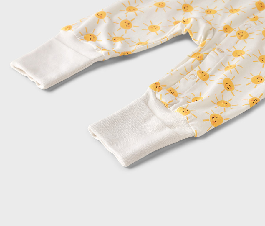 Detail detského overalu so žltým vzorom slnka a bielymi manžetami.