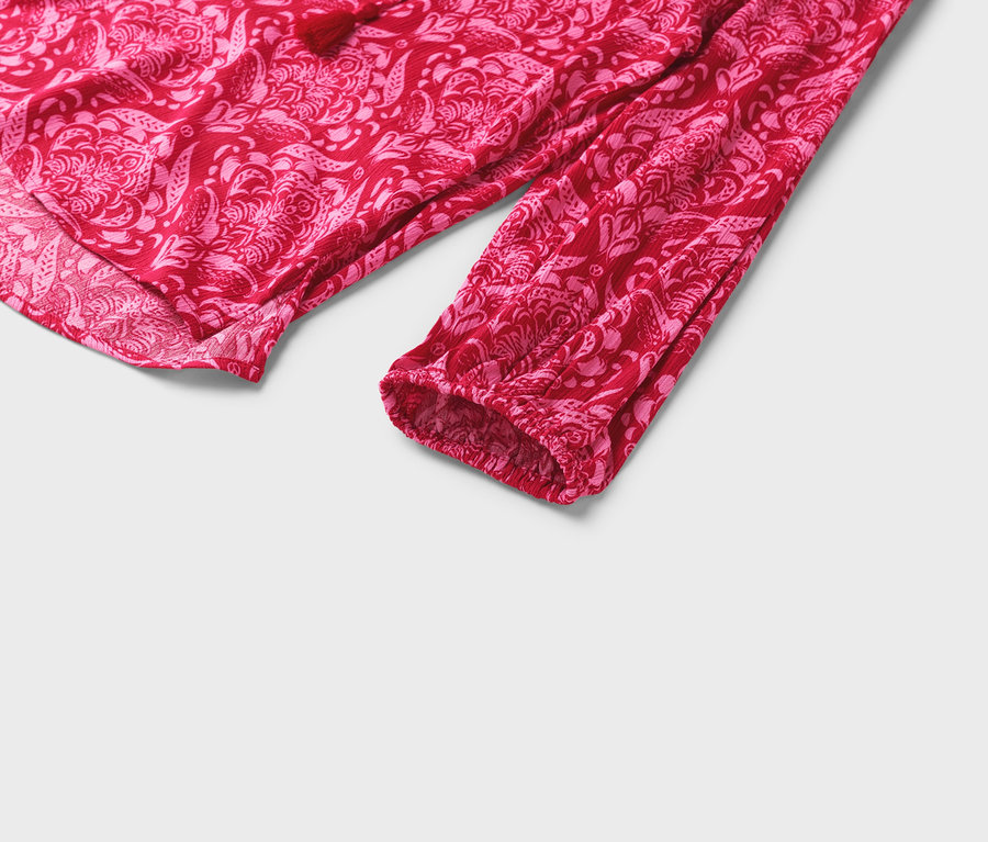 Detailný pohľad na červenú blúzku s ružovým kvetinovým vzorom a dlhými rukávmi.