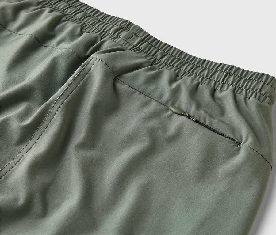 Detail olivovozelených nohavíc s elastickým pásom a vreckom na zips.