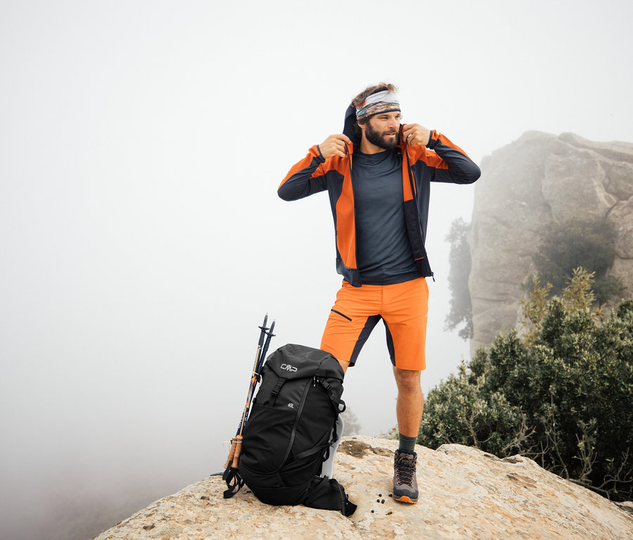 Muž stojí na skale s turistickým ruksakom CMP HAVRE, 40 litrov. Trekingové palice opreté o ruksak.