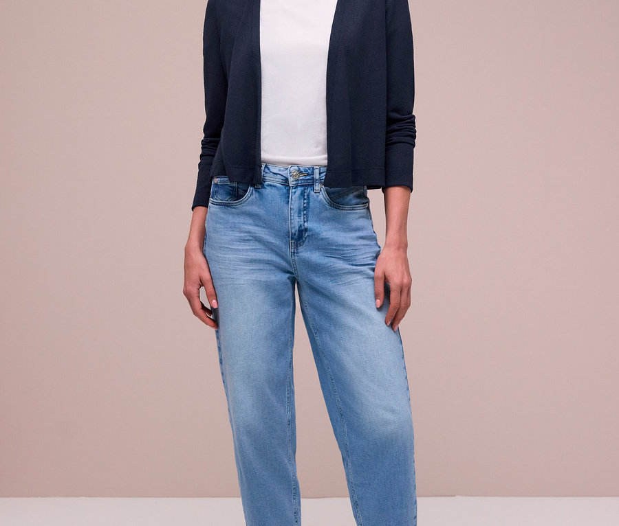 Žena má na sebe tmavomodrý kardigán Street One, biele tričko, svetlomodré džínsy, vzorovanú šatku a strieborné tenisky.