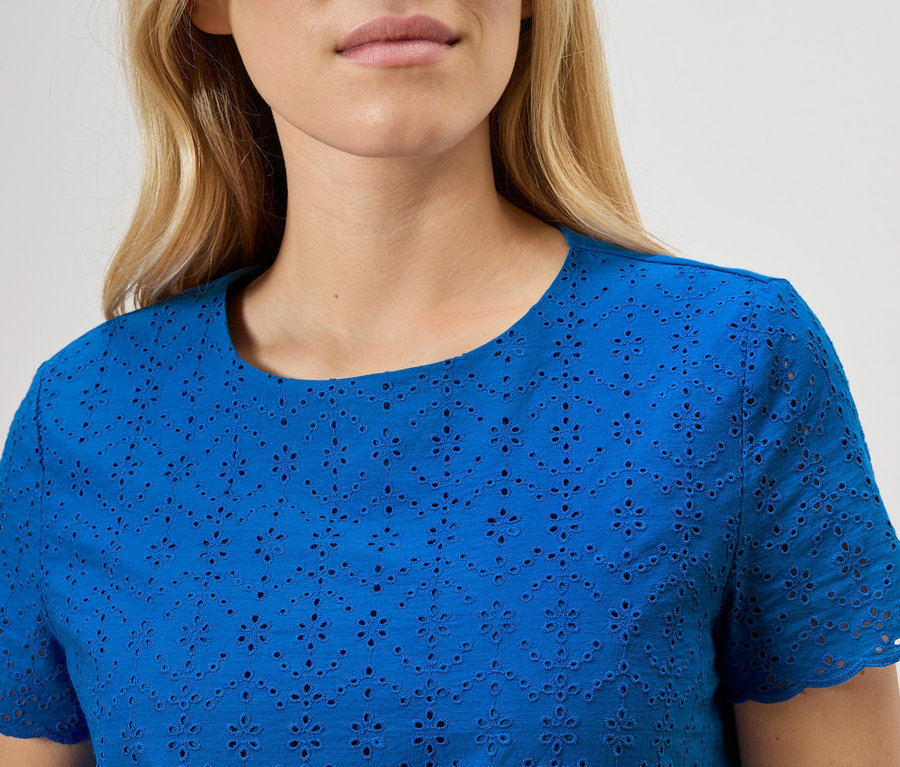 Detailný záber ženy v modrej blúzke s anglickou výšivkou.