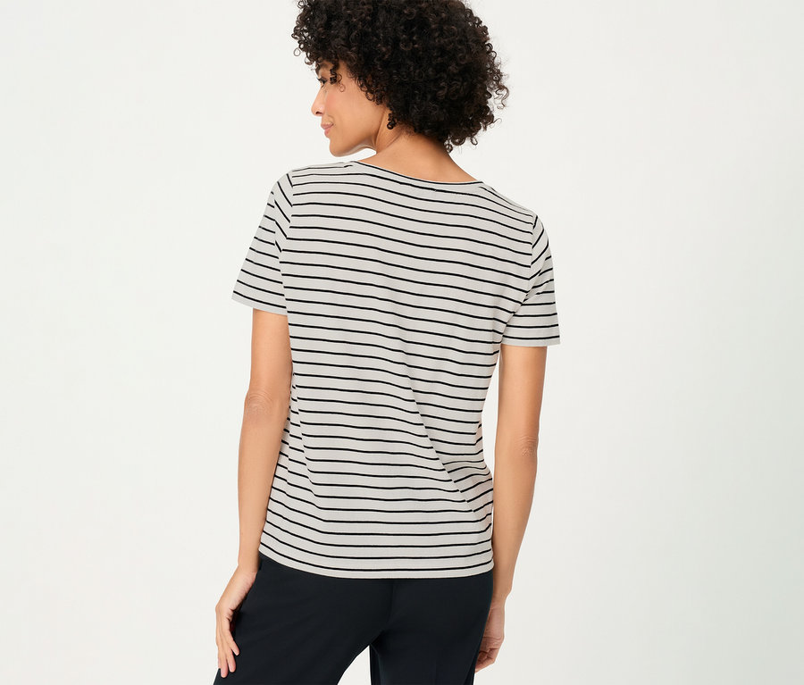 Pohľad zozadu na ženu s kučeravými vlasmi v tričku Olsen s čiernymi pruhmi a čiernych nohaviciach.