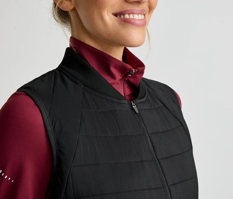 Žena v červenom tričku s dlhým rukávom a čiernej prešívanej veste na zips.