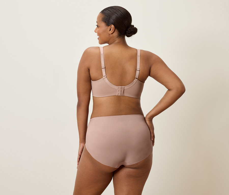 Žena zozadu, má na sebe telovú podprsenku a nohavičky, pričom má jednu ruku na boku.