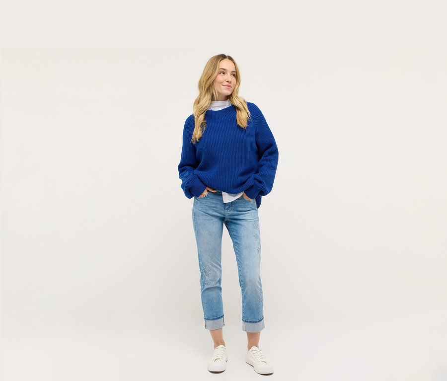 Žena má na sebe modrý pletený kabát a džínsy Angels Denim »Cira Boho«.