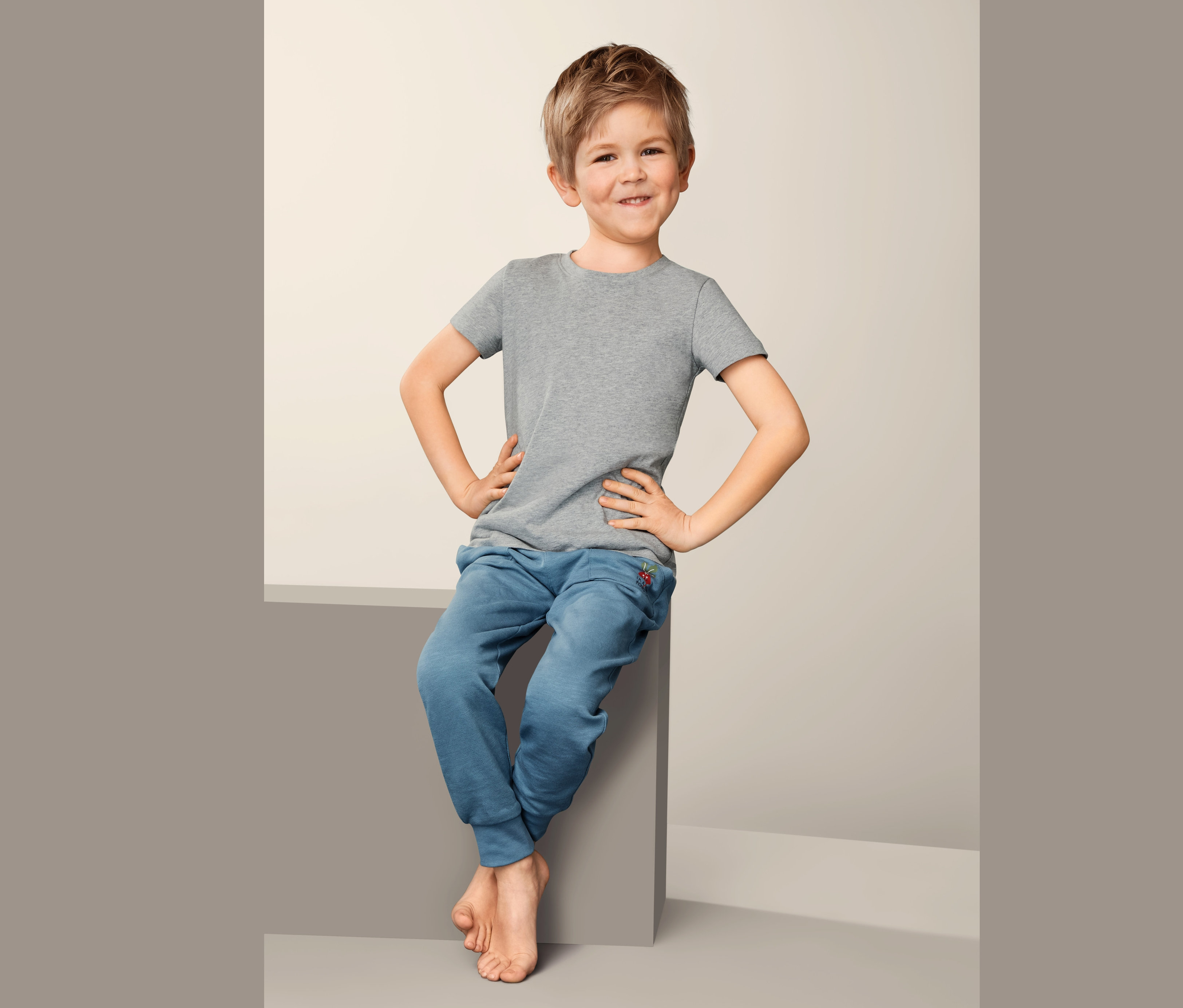 Chlapec sedí a má na sebe sivé spodné tričko (2 ks) a modré tepláky.