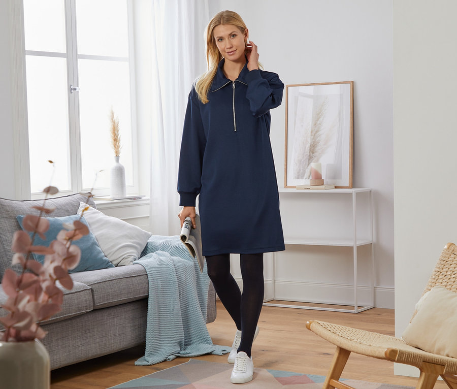 Žena pózuje v obývacej izbe a má na sebe teplákové šaty.