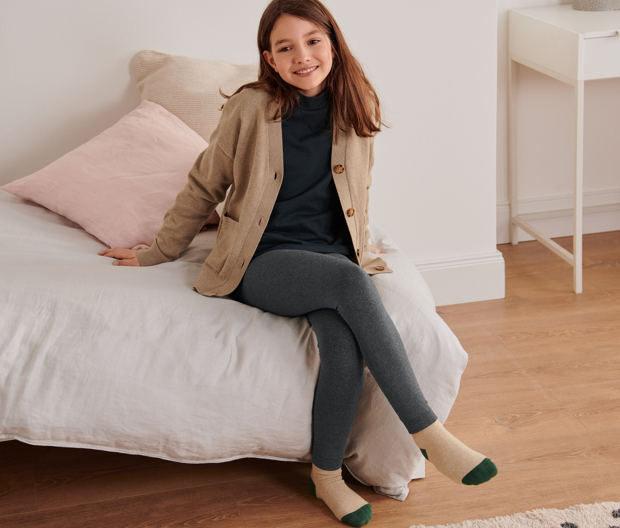 Dievča sedí na posteli a má na sebe detské termolegínsy.