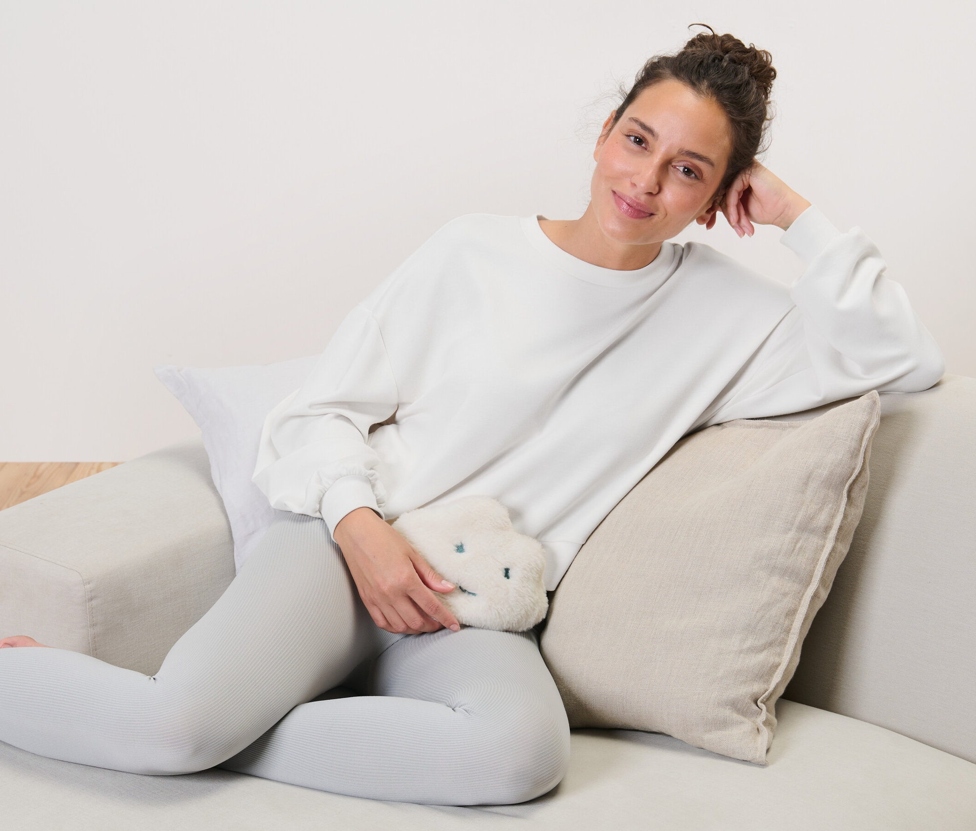 Žena sedí na gauči a drží ohrievací vankúšik s čerešňovými kôstkami v tvare obláčika.