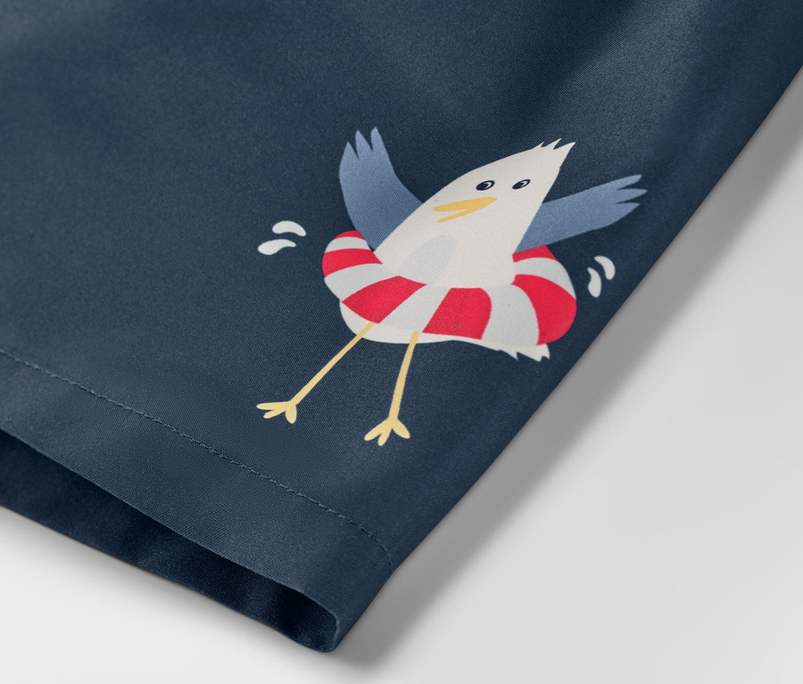 Detail detských šortiek na kúpanie s námorníckym motívom a potlačou čajky v záchrannom kruhu.