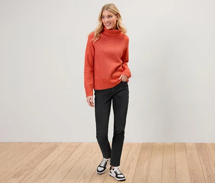 Žena pózuje v oranžovom svetri a čiernych slim džínsoch – Fit »Emma«.