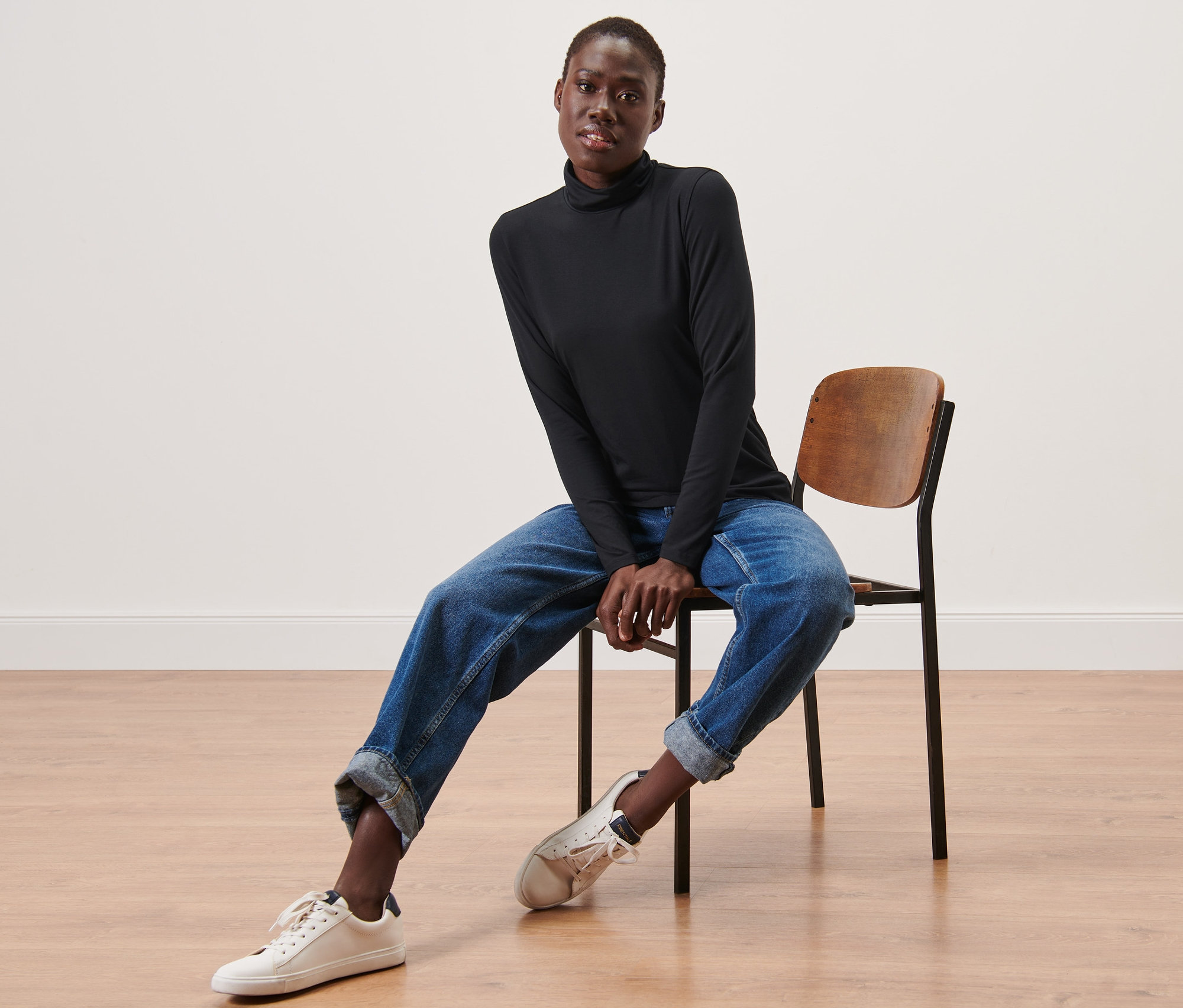 Žena sedí na stoličke a má na sebe čierne tričko s rolákovým golierom.