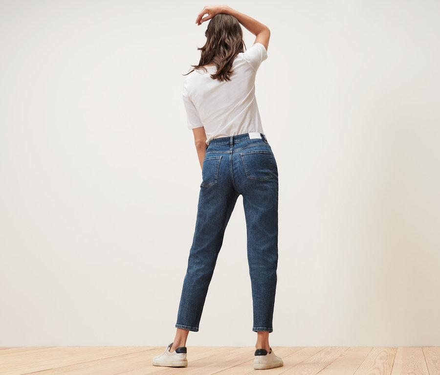 Žena pózuje v Mom džínsach – strih »Nyla« a bielom tričku.