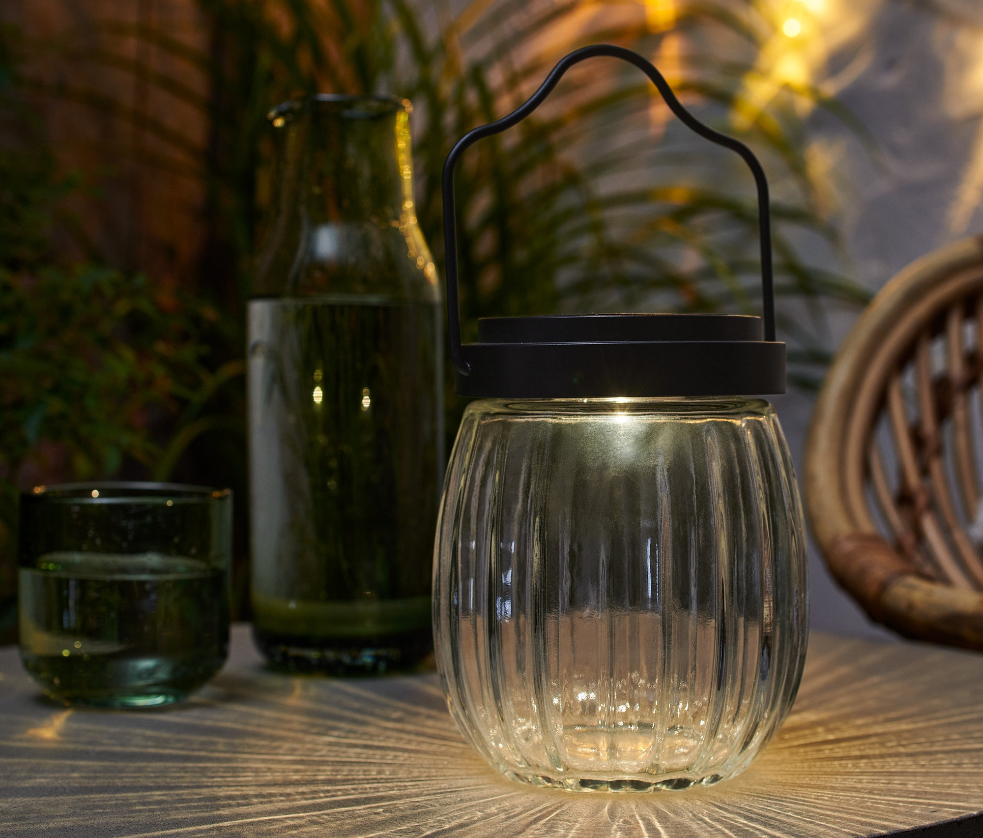 Sklenené solárne svietidlo stojí na stole vedľa pohára a fľaše.