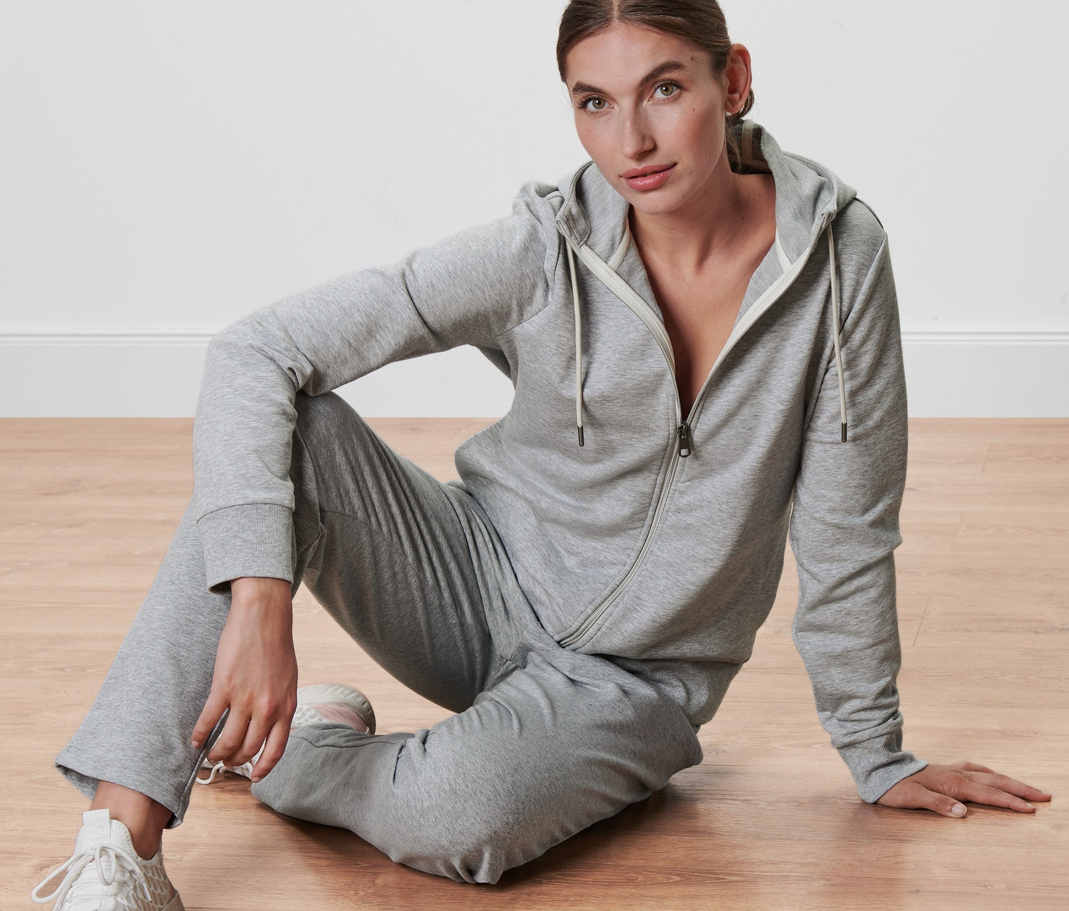 Žena sedí na podlahe a má na sebe sivú mikinu.