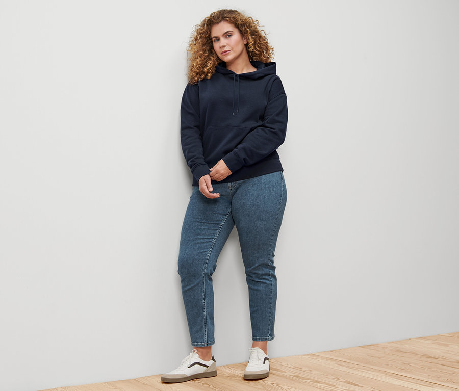 Žena stojaca pri stene má na sebe tmavomodrú mikinu s kapucňou.