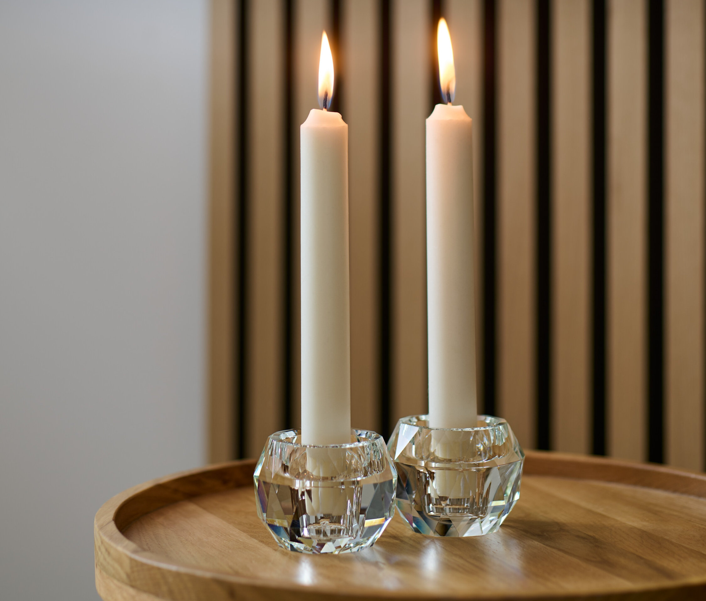 Dva sklenené svietniky s horiacimi sviečkami na drevenom stole.