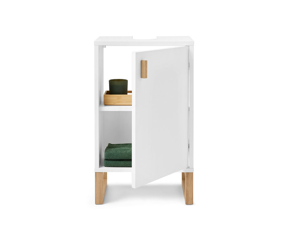 Malá biela umývadlová skrinka s dvierkami, dvere sú otvorené, vnútri je zelená sviečka a zelené uteráky.