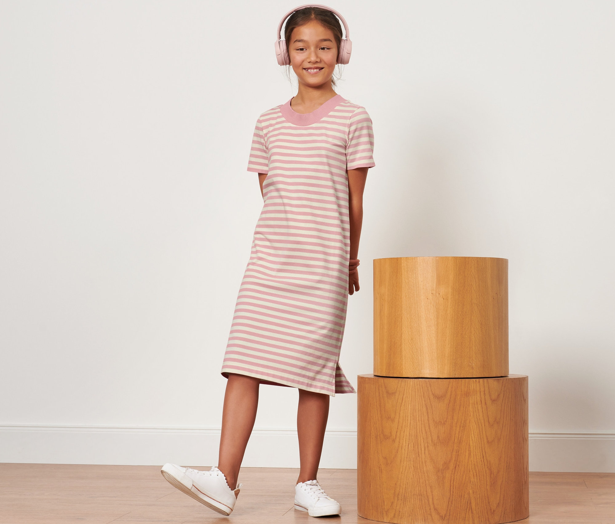 Dievča s ružovými slúchadlami stojí v pruhovaných detských džersejových šatách.