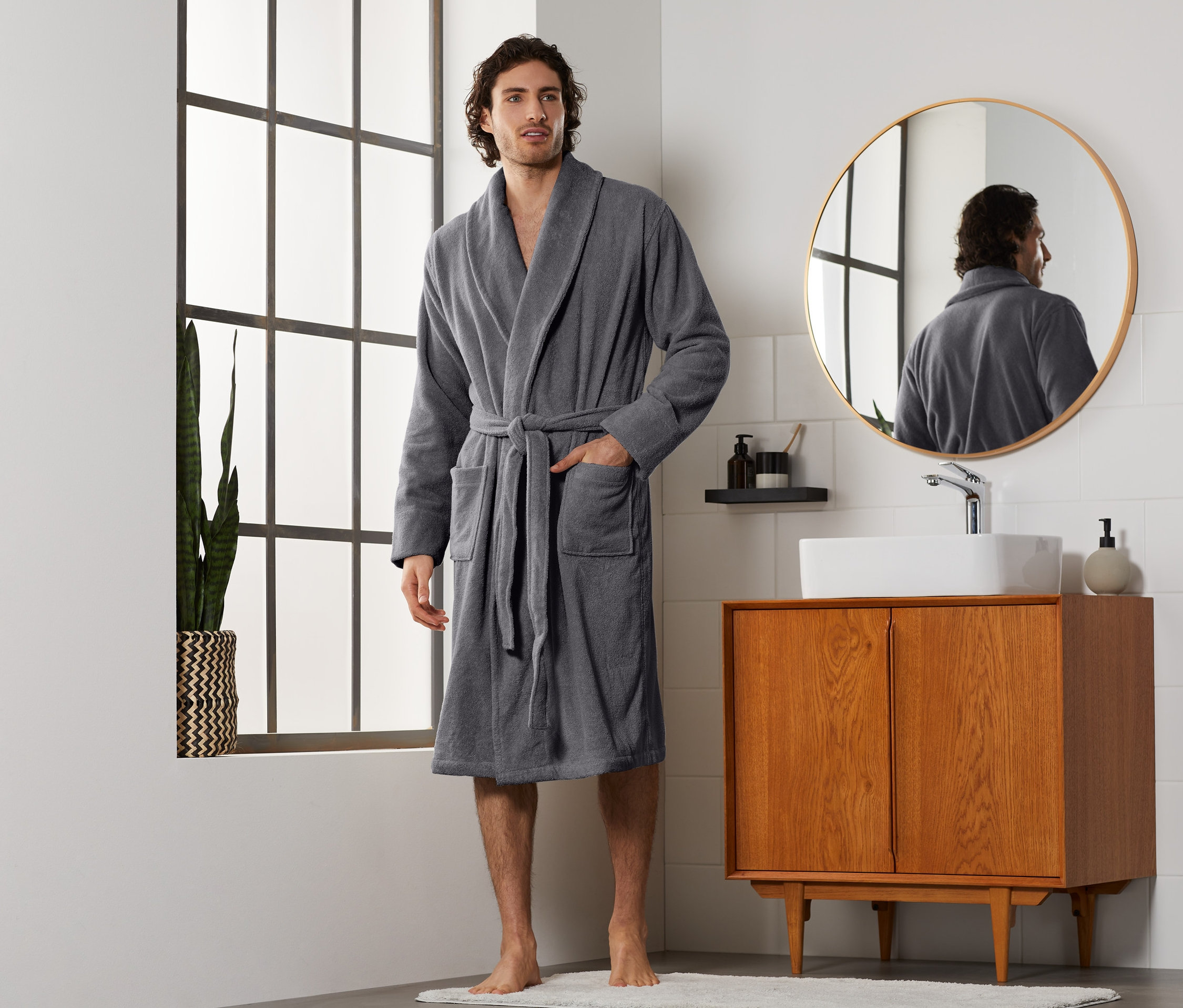 Muž v sivom pánskom župane stojí v kúpeľni.