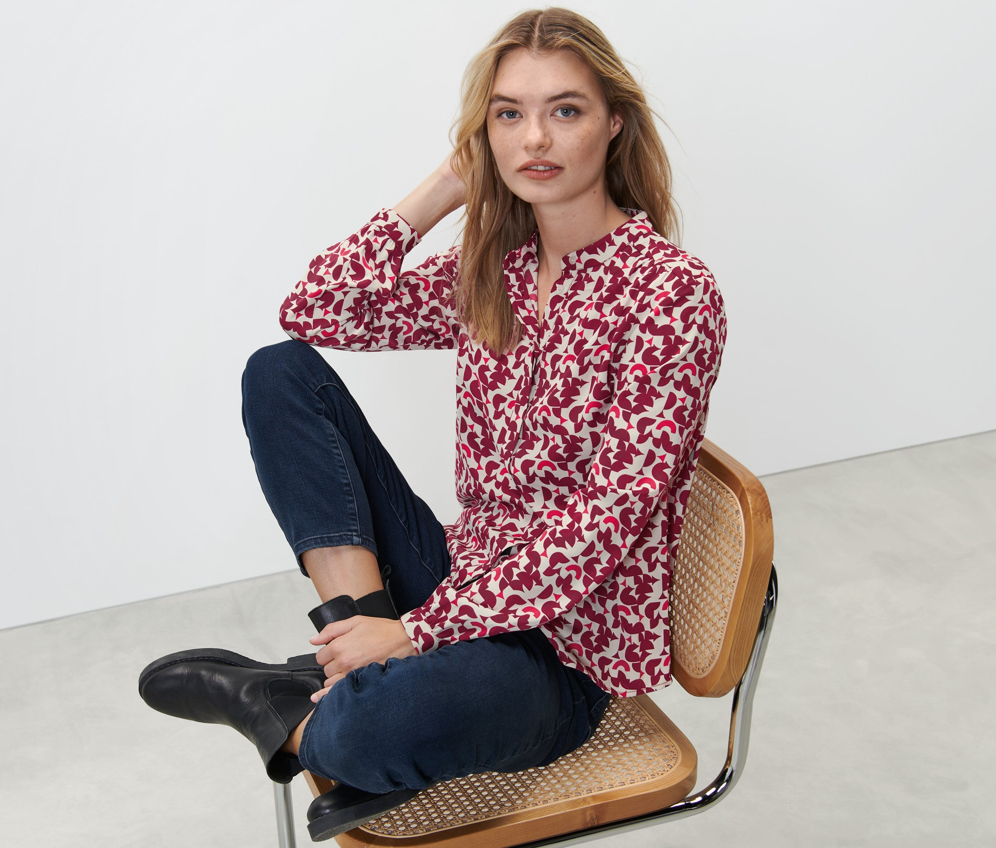 Žena sedí na stoličke a má na sebe blúzku s potlačou.