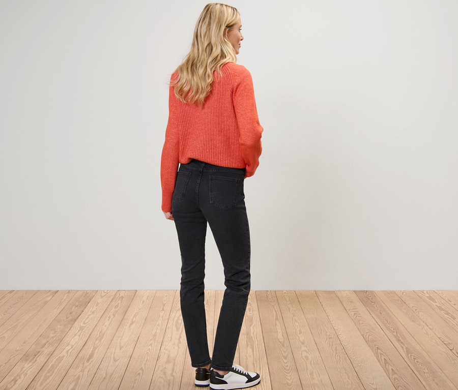 Blondínka pózuje chrbtom, má na sebe oranžový sveter a slim džínsy – Fit »Emma«.
