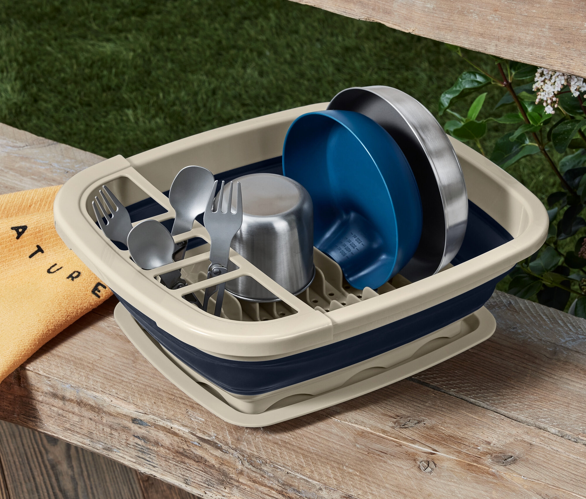 Skladací odkvapkávač na riad s riadom a príbormi na drevenom stole.