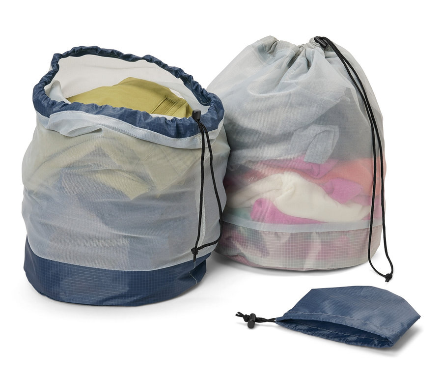 Dve outdoorové vrecká zo sieťoviny, jedno otvorené a plné oblečenia, druhé zatvorené, a prázdne vrecko.