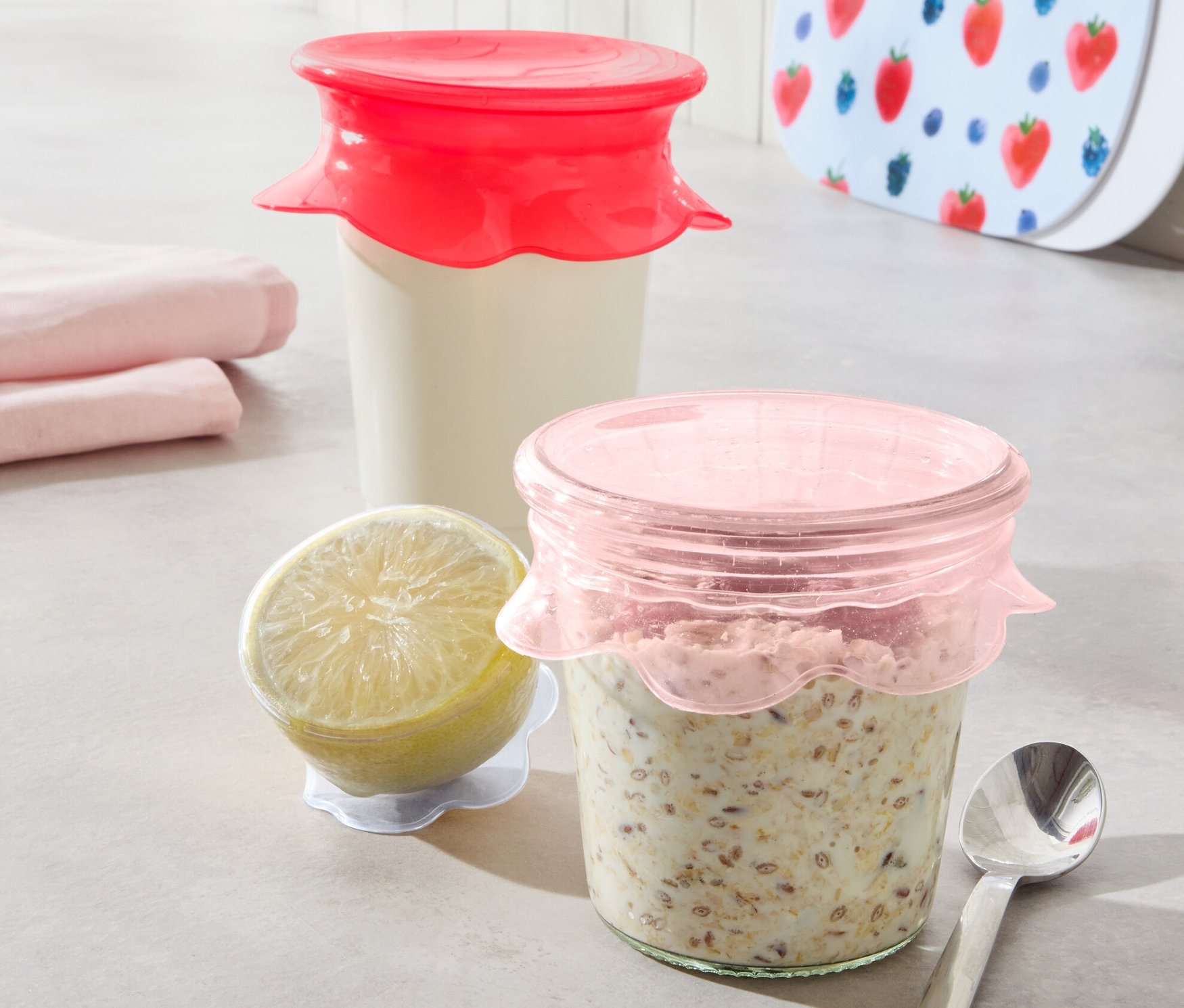 Dva poháre s obsahom sú zakryté 3 silikónovými viečkami na udržiavanie čerstvosti. Vedľa je citrón a lyžica.