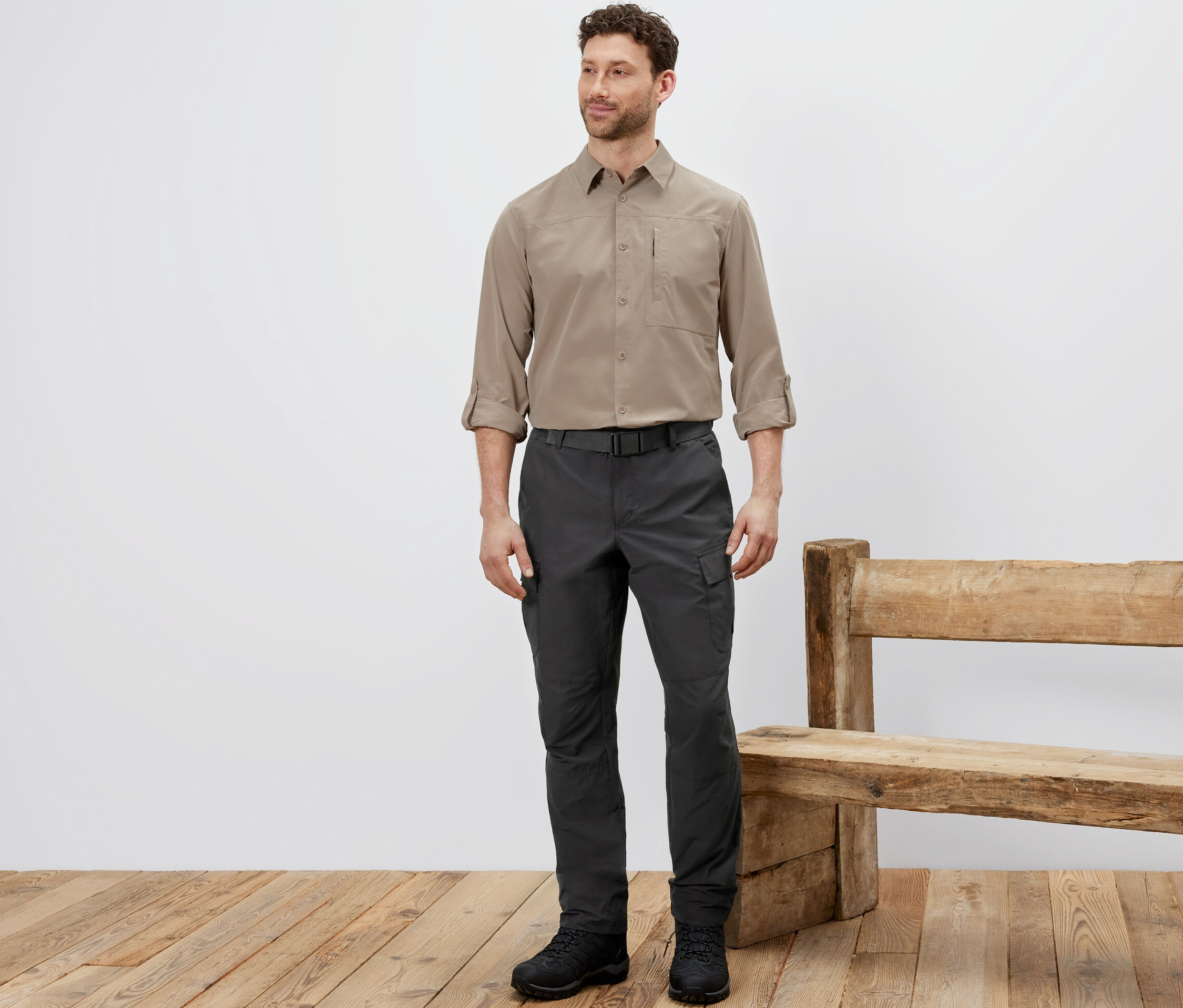 Muž stojí a má na sebe outdoorové nohavice s ochranou proti komárom, béžovú košeľu a čierne topánky.