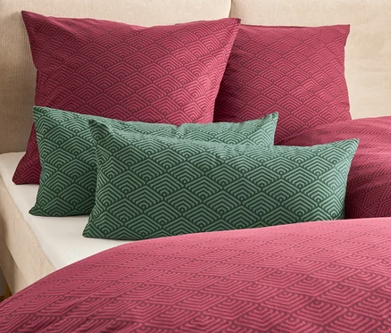 Na posteli sú dva vínové a dva zelené vankúše s geometrickým vzorom.