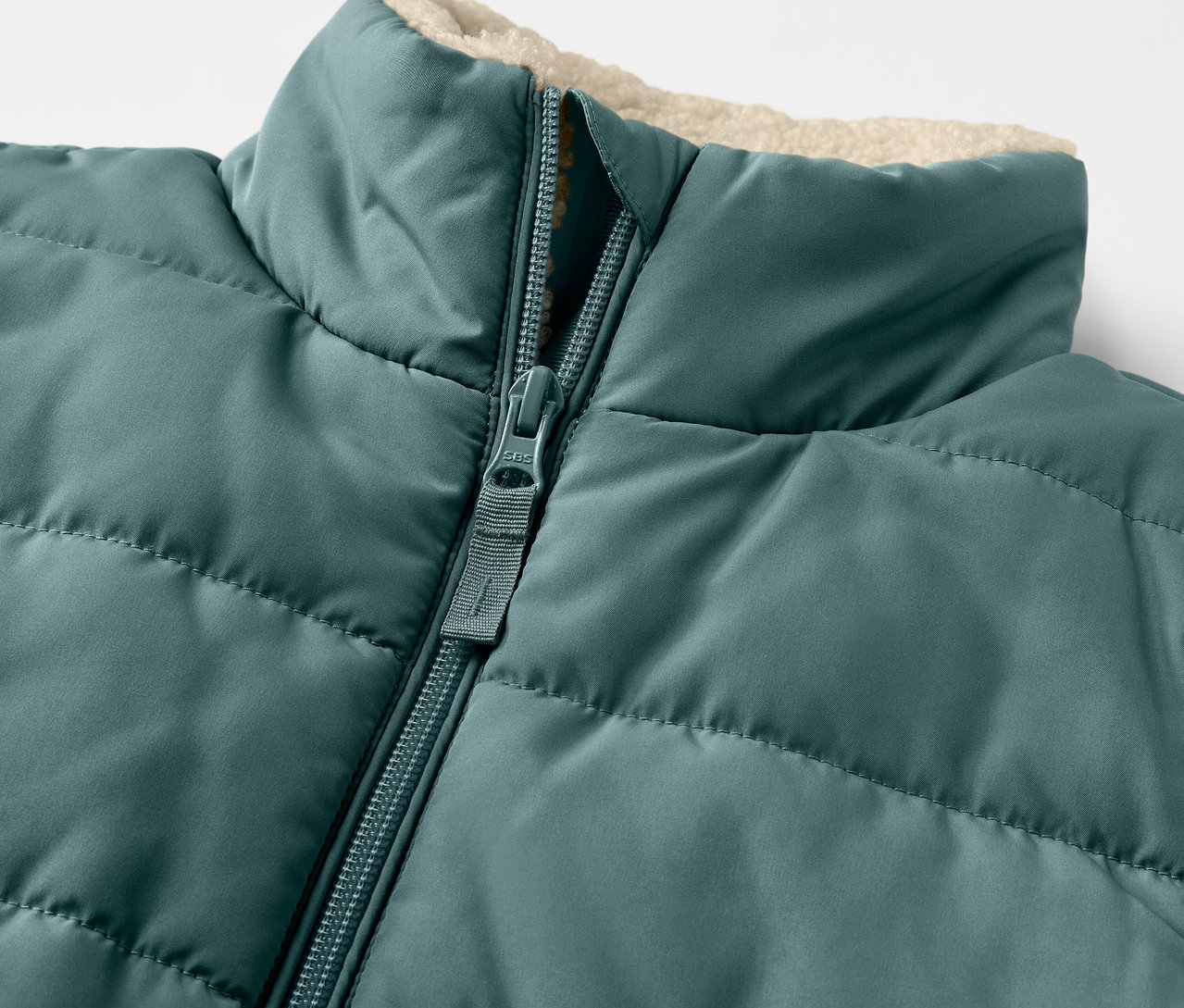 Detail detskej prešívanej vesty s plyšovou podšívkou a zipsom.