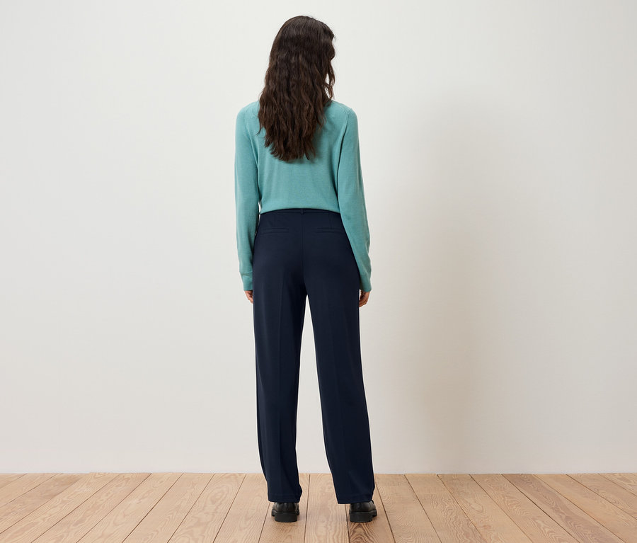 Zozadu je vidieť žena s tmavohnedými vlasmi v tyrkysovom svetri a tmavomodrých nohaviciach.