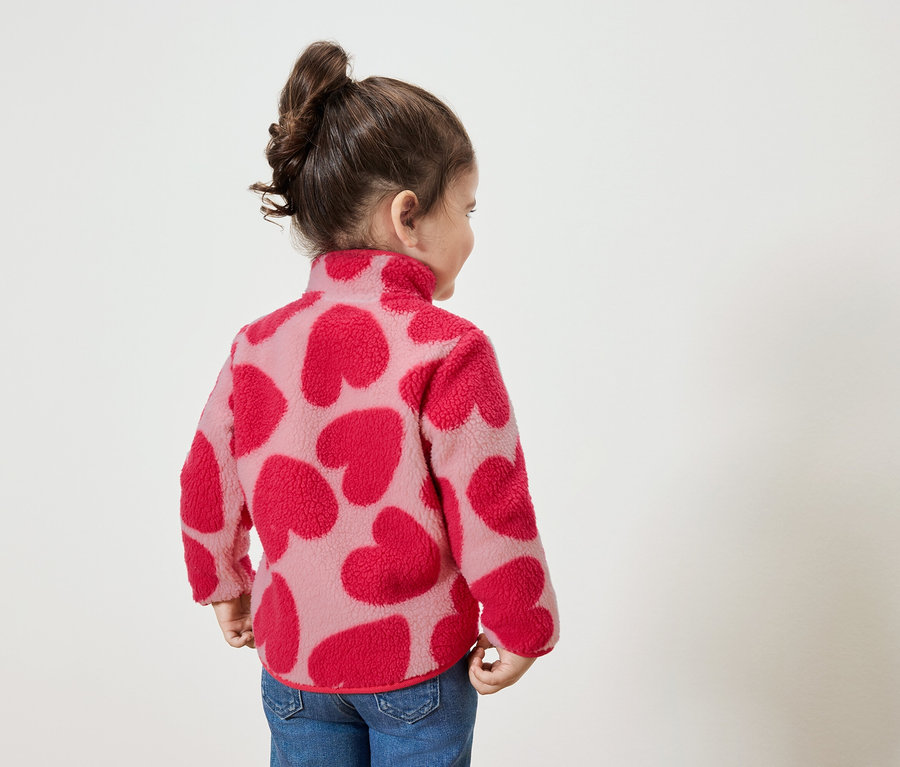 Malé dievčatko v mikine s červenými srdiečkami, pozerá sa doprava.